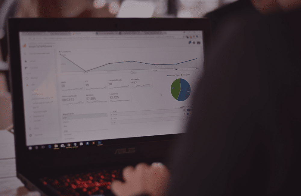 Uma pessoa de costas mexendo em um notebook com a página de gráficos do Google Analytics