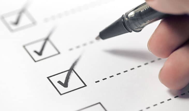 mão segurando caneta assinalando checklist em papel branco