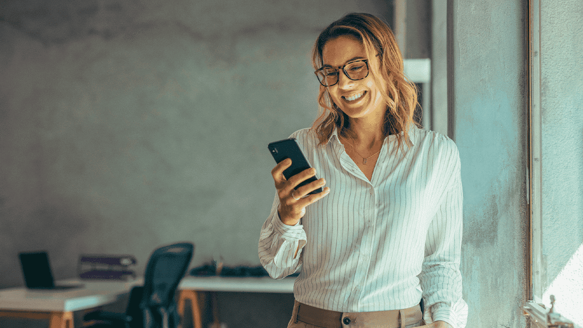 mulher sorrindo e olhando para celular em escritório