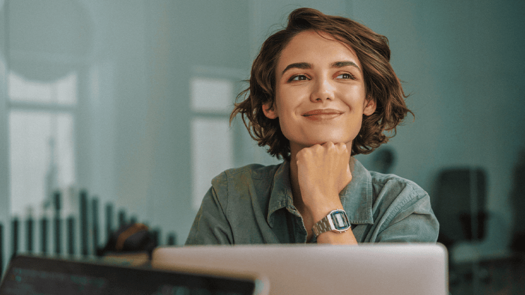mulher sorrindo e refletindo enquanto trabalha em laptop