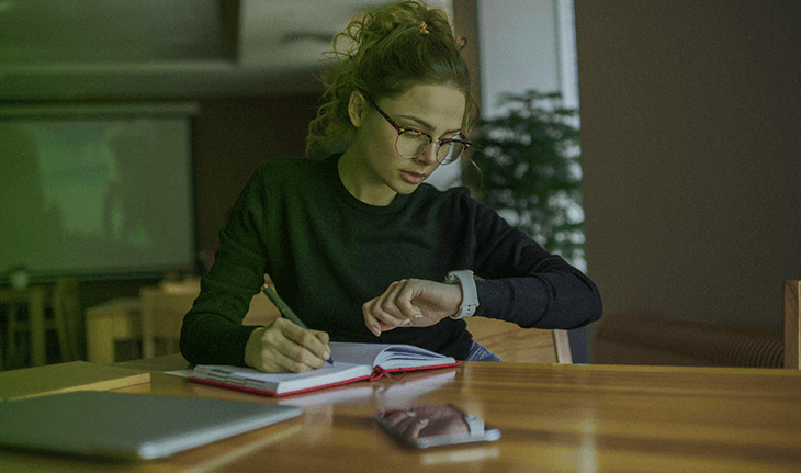 mulher escrevendo em caderno e olhando relógio de pulso
