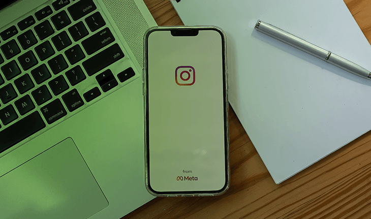 celular com logo do Instagram sobre mesa com laptop e caderno