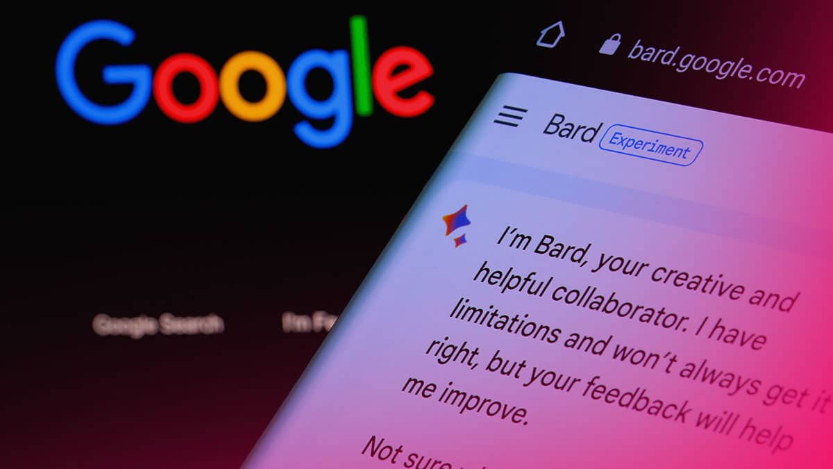 mão segurando celular com Google Bard ao fundo computador com página de pesquisa